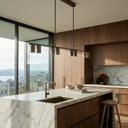 A modern minimalist kitchen scene featuring a long horizontal linear pendant light with six cylindrical textured shades hanging above a wooden slatted island and a beige wall.
